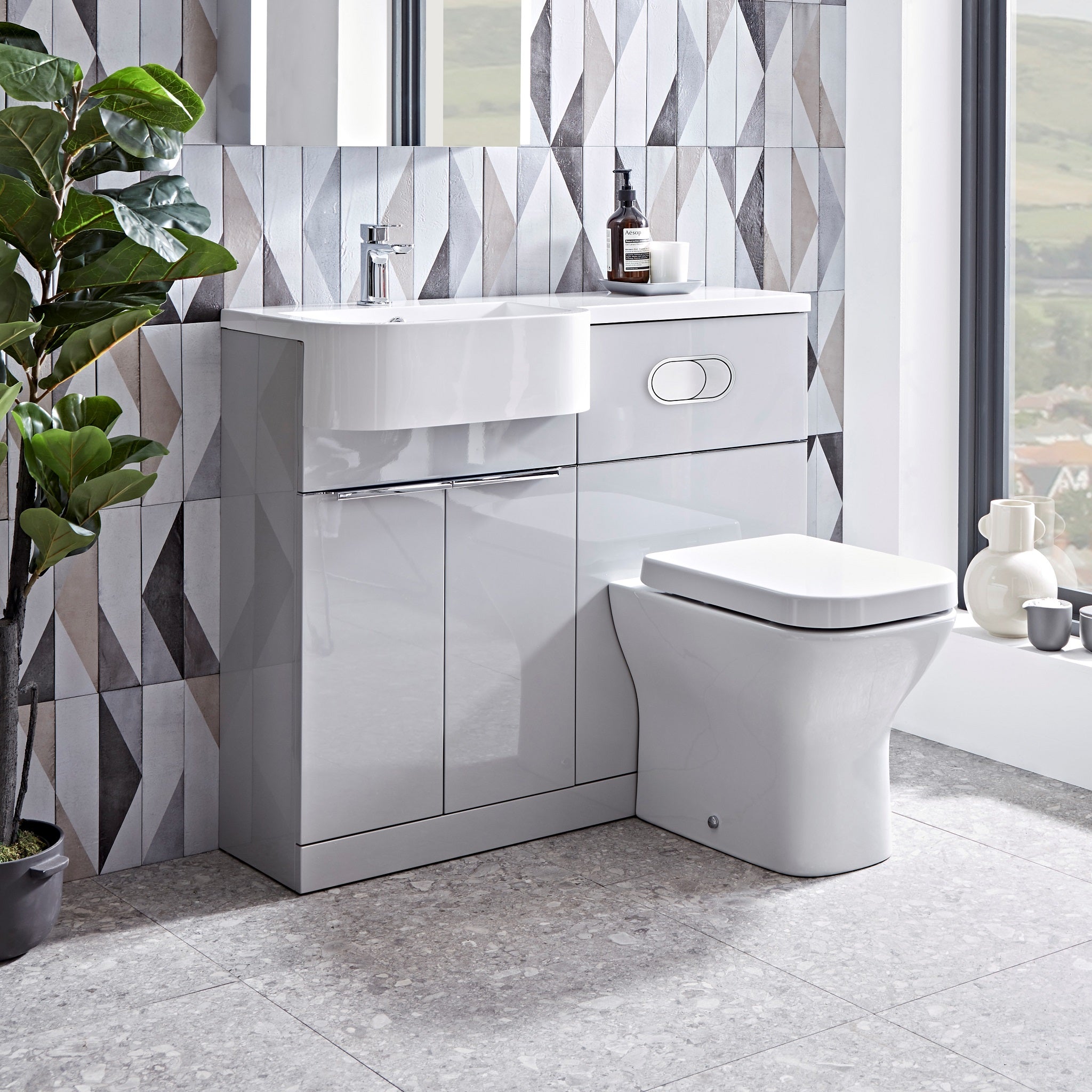 Tavistock Match 1000mm Combination Unit - Gloss Light Grey (L or R Hand) unit against wooden wallpaper design underneath a mirror with a plant fading off the left side MATLG