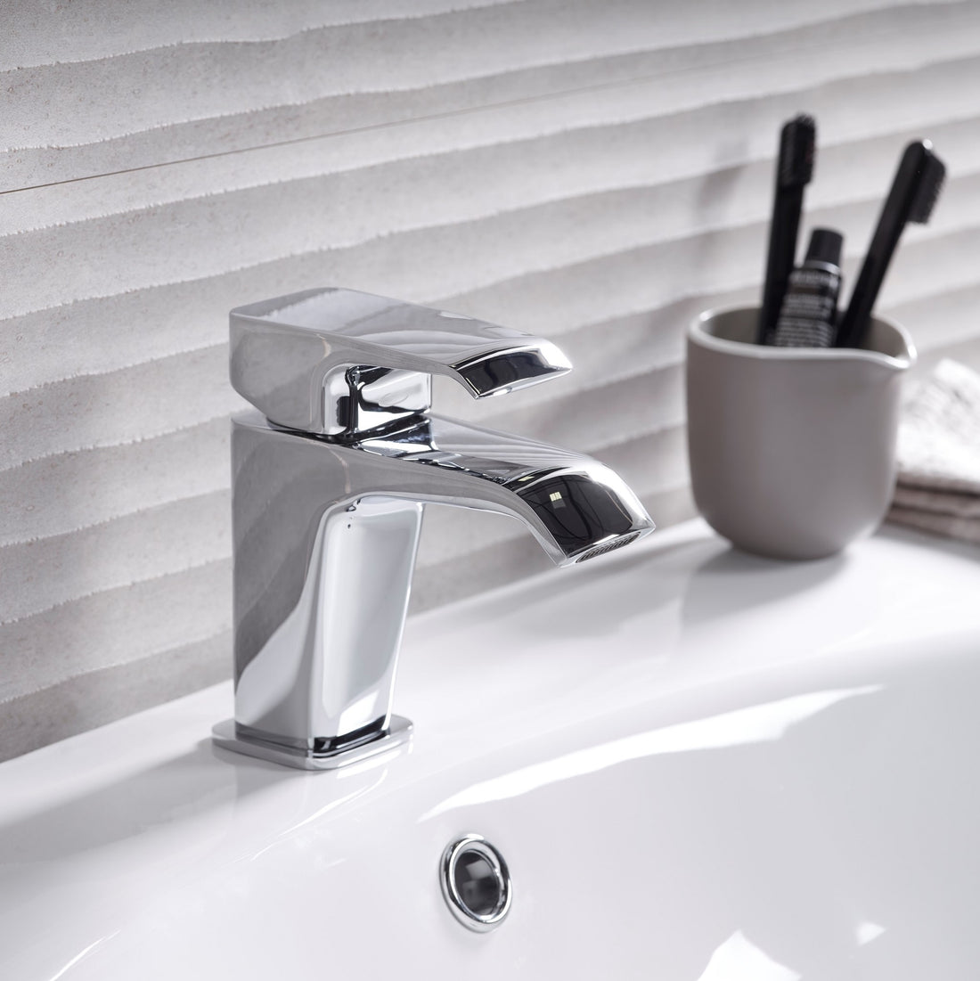 Tavistock Adapt Basin Mixer With Click Waste - Chrome next to a tooth brush hold in front of tiles TAD11