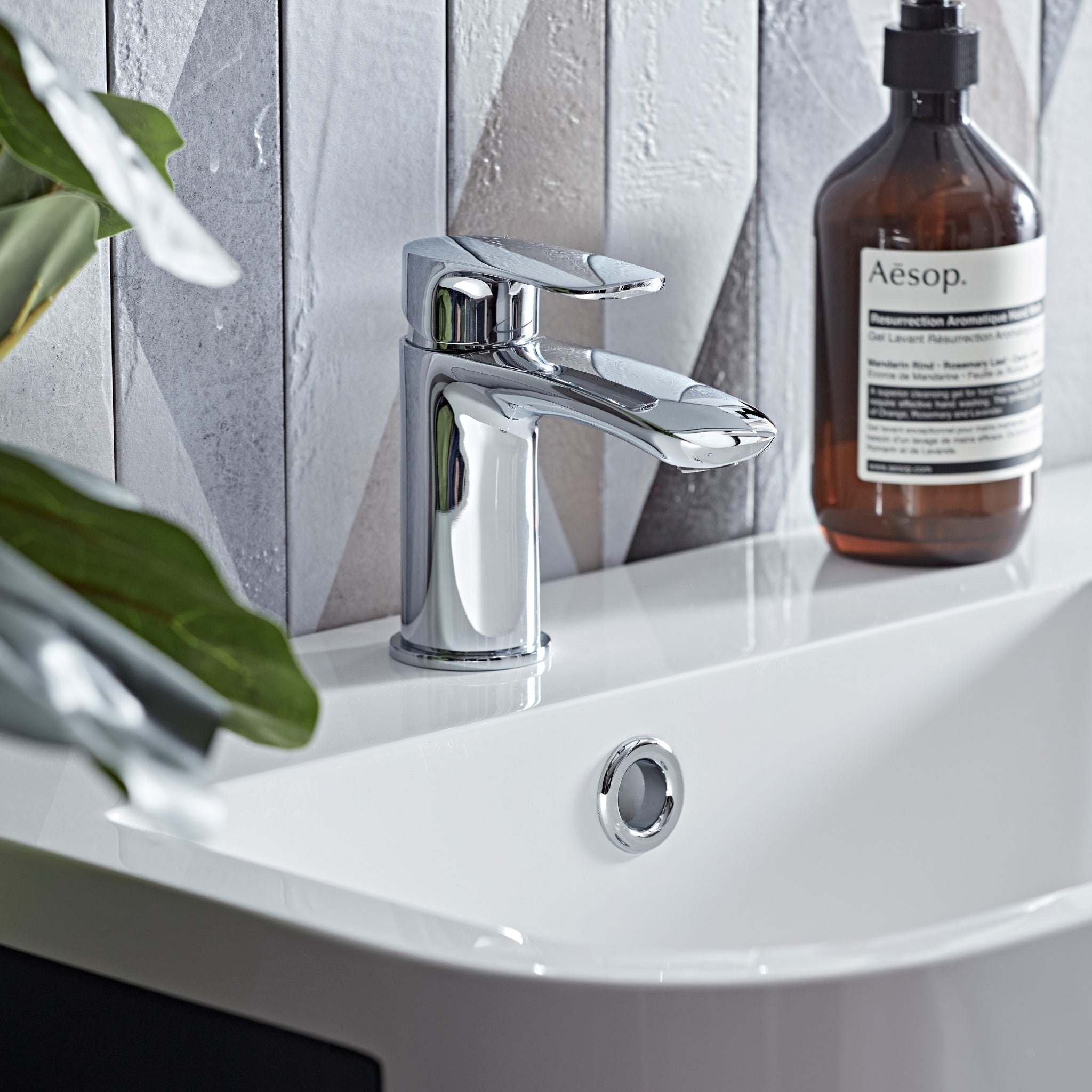 Tavistock Avid Basin Mixer With Click Waste in front of wood design with bottle on basin TAV11